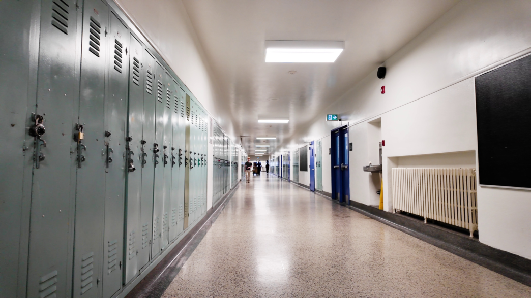 A mostly empty school hallway, with lockers on the left and classrooms on the right.