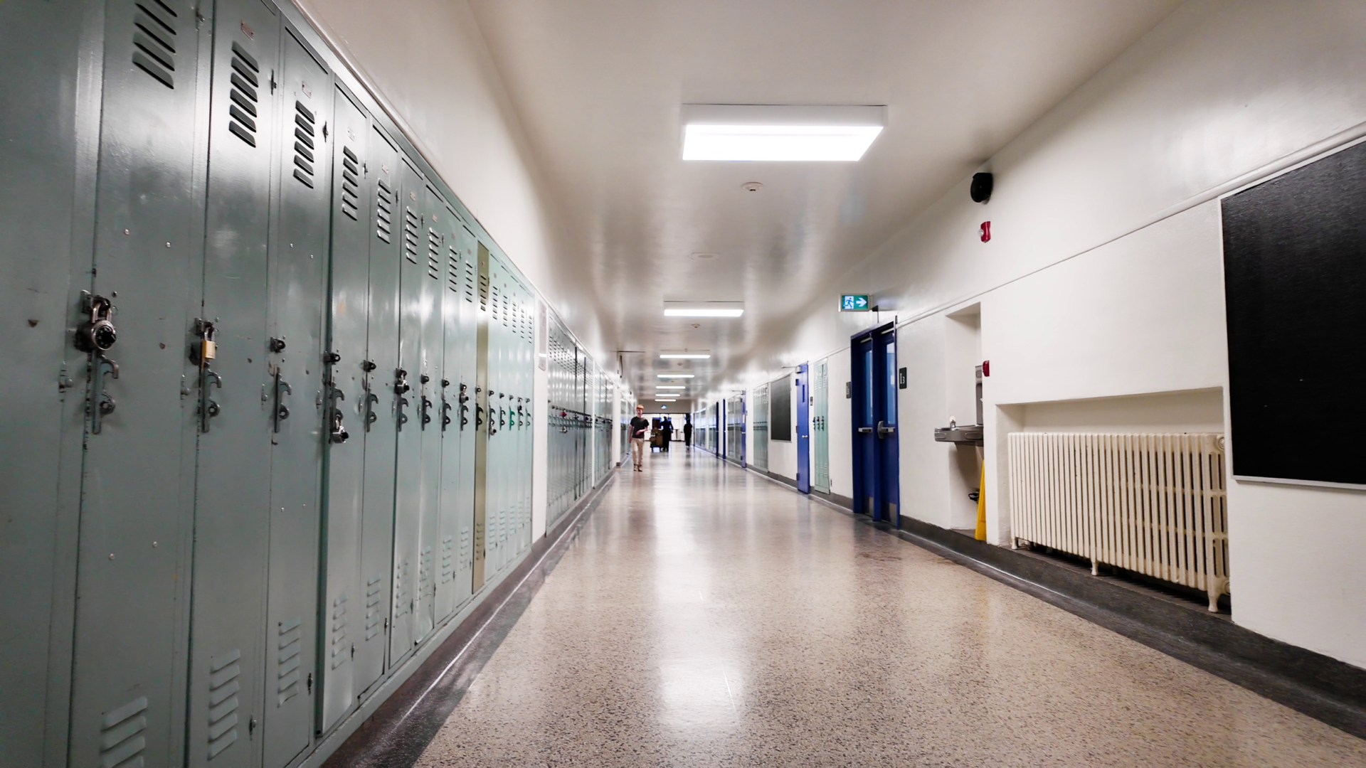 A mostly empty school hallway, with lockers on the left and classrooms on the right.