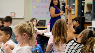 Litchfield Elementary School student raises hand in class while teacher looks on. (Katie Wilcox/The Beam)